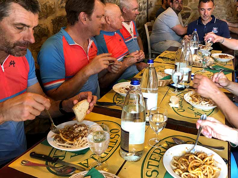 Cyclists in an Italian trattoria eating a mid ride lunch of Pici con ragu