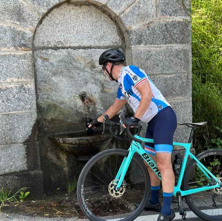 A rider filling up his bottle at a fountain in the Italian mountains