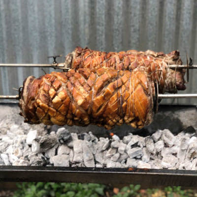Two porchetta being cooked on the spit over charcoal