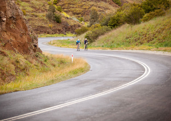 two cyclists riding up a twisting hill near daylesford