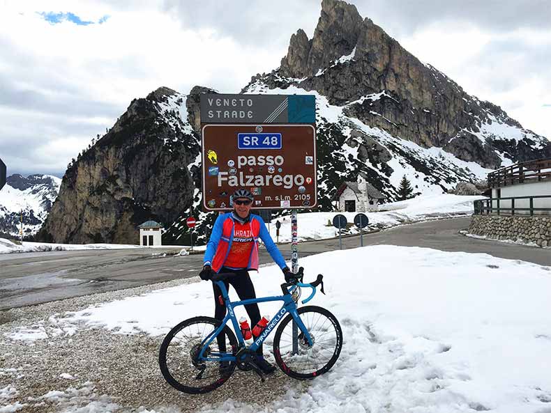 a cyclist standing in front of the Sing of Passo Falzarego