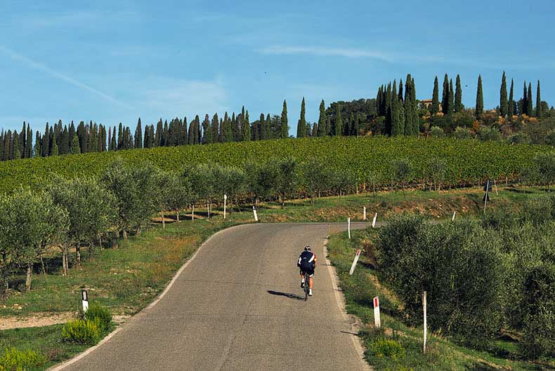 a rider cycling up a steep hill in Tuscany
