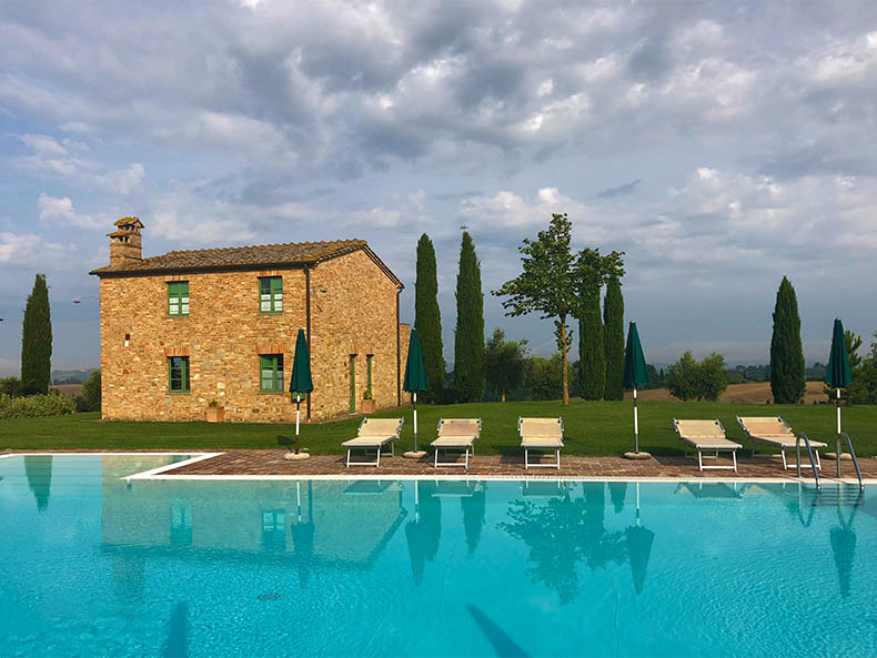 A pool, stone house and cypress pines in Tuscany