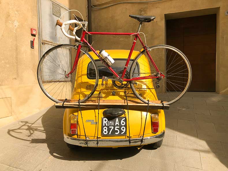 A yellow Fiat 500 with a vintage steel bicycle on the back