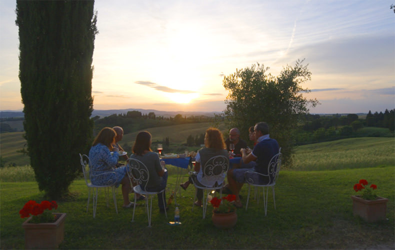 a group of people having a glass of wine and antipasti as the sun sets over the Tuscan Landscape