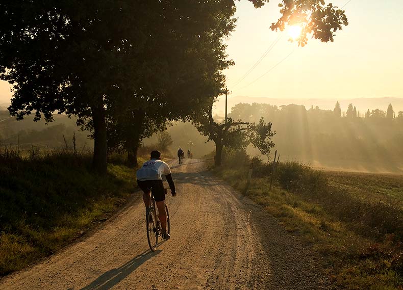 A cyclist riding on a gravel road at sunrise