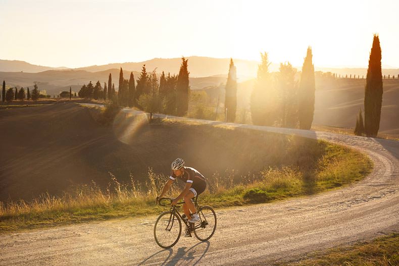A cyclist riding on a gravel road in Tuscany at sunset