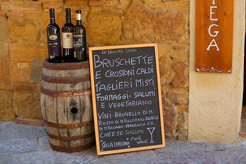 A wine barrels with bottles sitting on top and a chalkboard sign with lunch specials in Tuscany