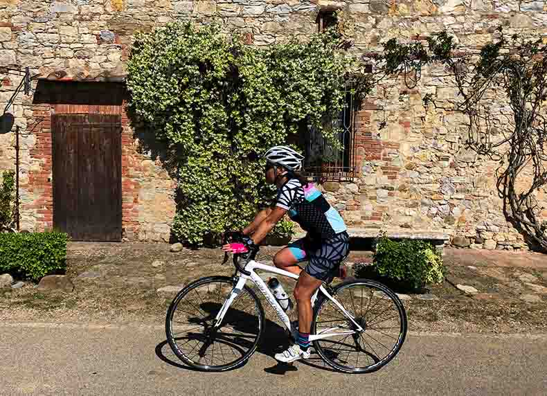 a woman cycling past a jasmine covered stone house in Tuscany