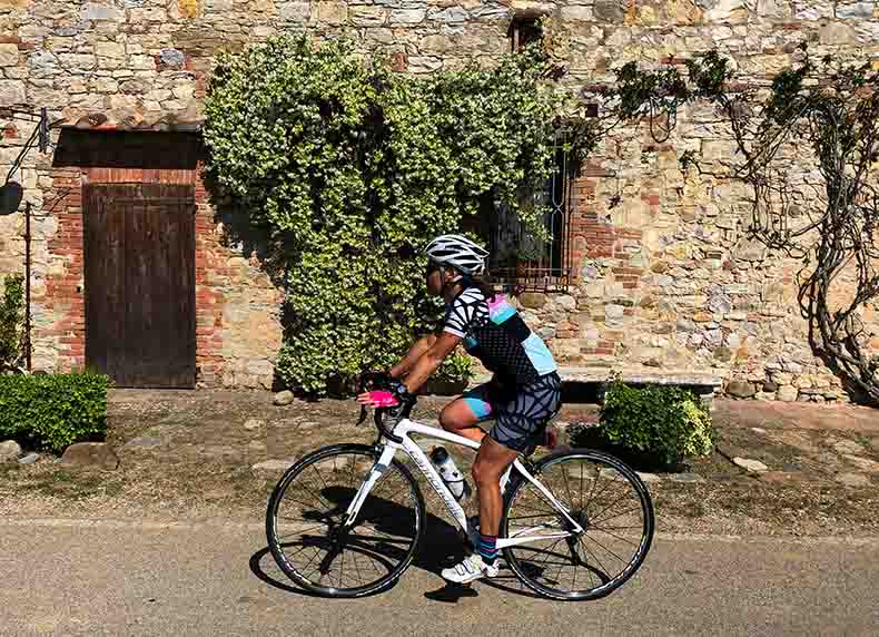 a woman cycling past a jasmine covered stone house in Tuscany