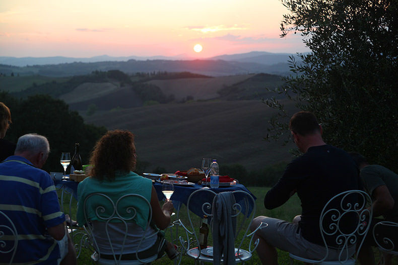 A group of people have a glass of wine and watch the setting Tuscan Sun