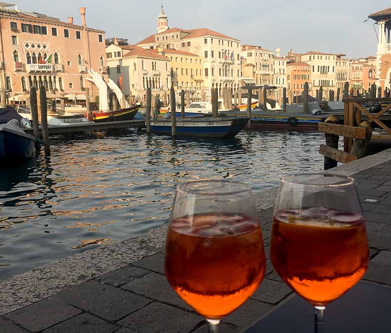 A glasses filled with aperol spritz and a view of the grand canal in Venice