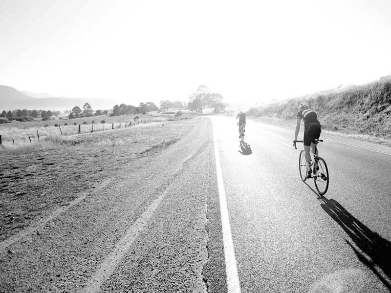 Two riders cycling in the open country landscape of Bright