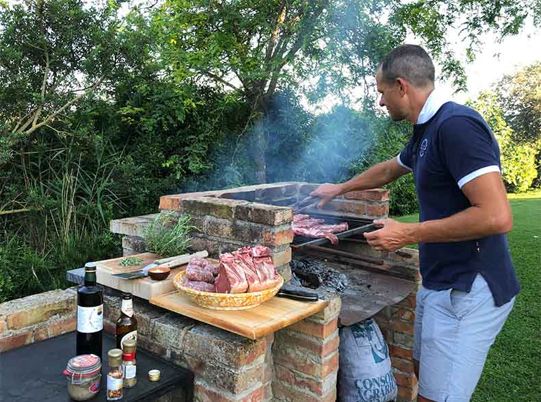 a man cooking a BBQ with charcoal and fire in Tuscany