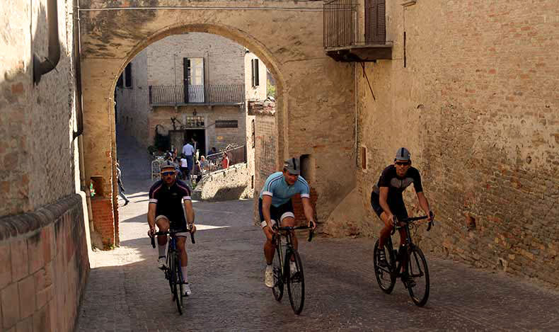 Three cyclists riding steel Stelbel bikes through a small town in Piemonte