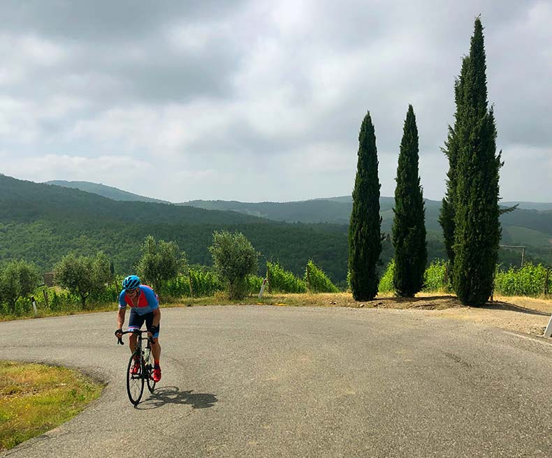 A cyclist riding past three cypress pine trees in Tuscany