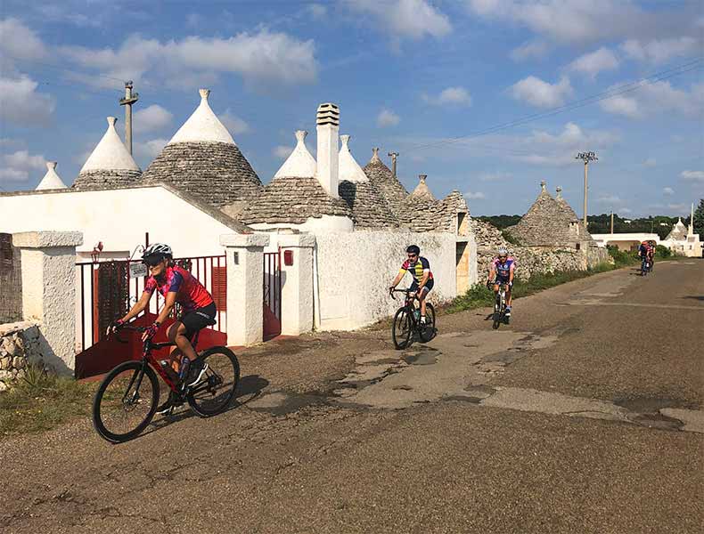 A group of cyclists riding past a Trulli in Puglia