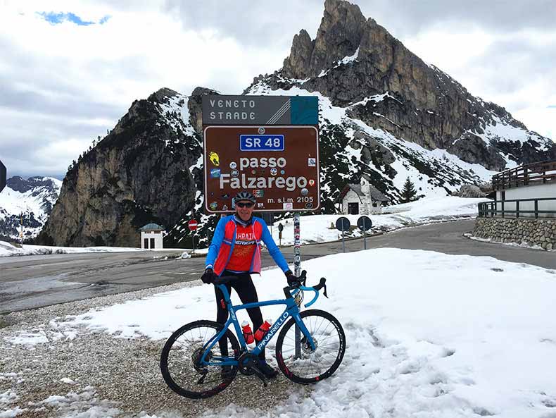 A man with his bicycle standing in front of the Passo Falzarego sign
