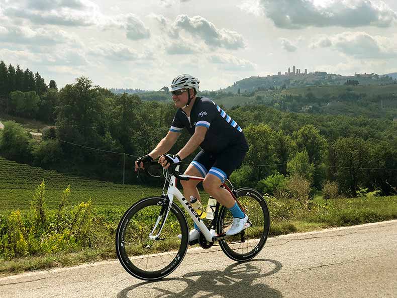 A cyclist riding in Tuscany with the towers of San Gimignano in background
