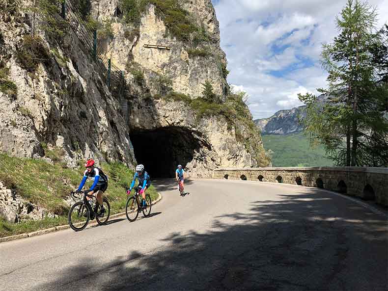 three cyclists riding through a tunnel on the climb to Passo Falzarego