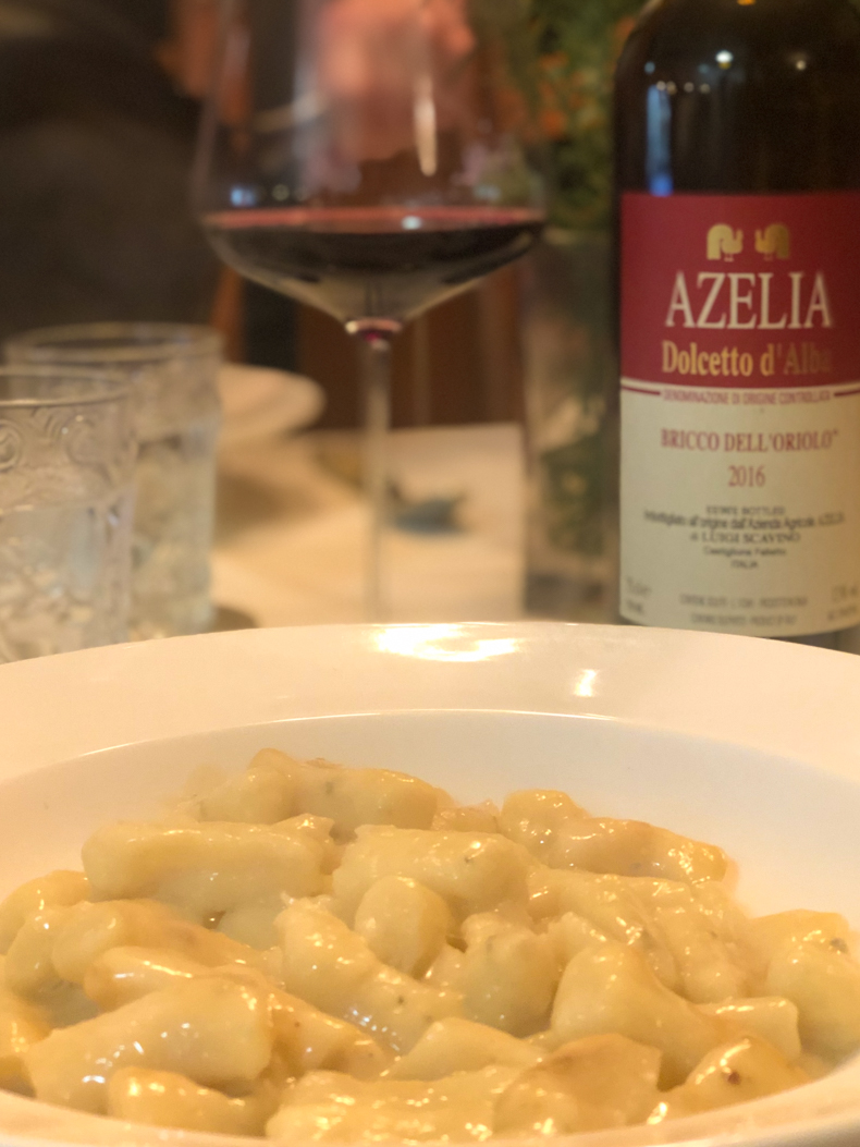 a bowl of gnocchi with a gorgonzola sauce and a glass of red wine