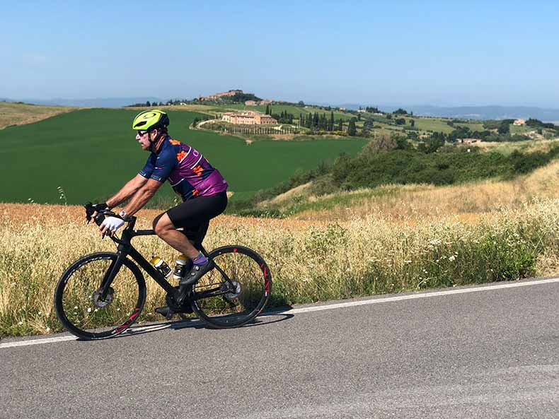 a man cycling along a road through the Tuscan landscape