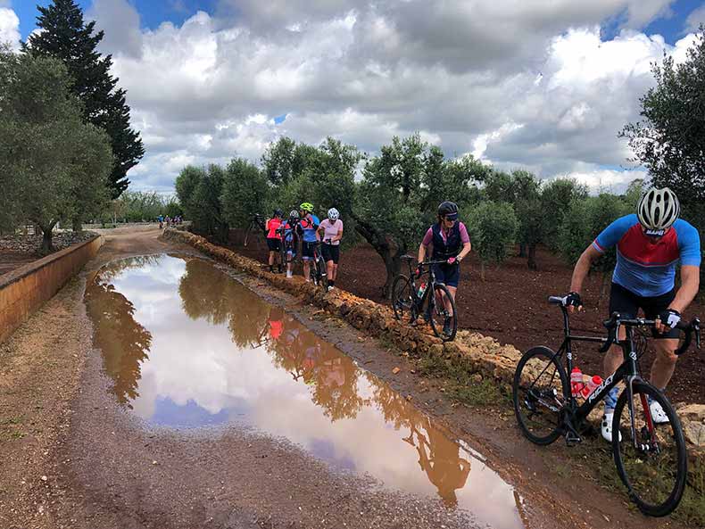 Cyclists carrying their bikes around a very big puddle