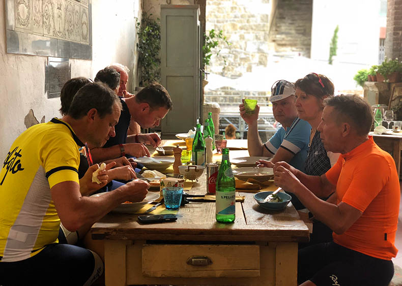 A group of cyclists at one table have a mid ride lunch