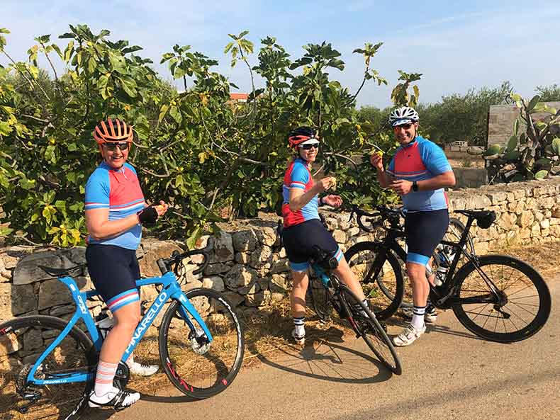 Three riders picking figs from a tree during a cycling holiday in Pugliua