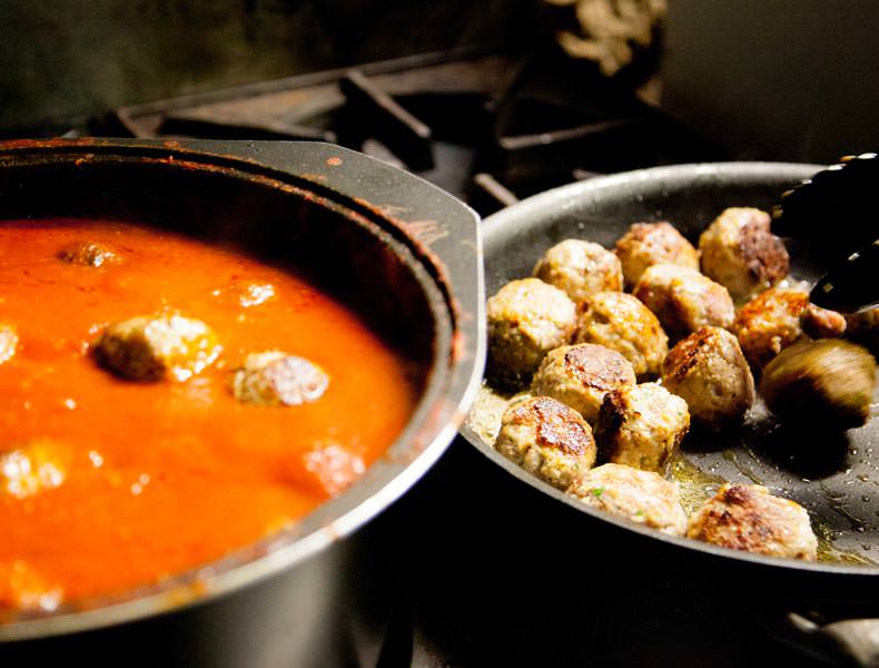 Two pots ona stove filled with meatballs and a tomato sugo