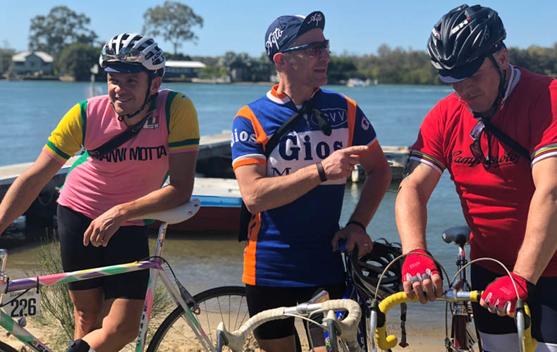 Three cyclists in woolen jerseys and steel bikes near the water