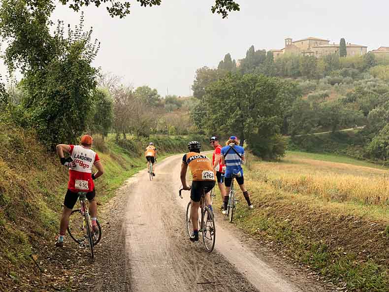 A group of riders on a gravel road with a stone hamlet in the distance