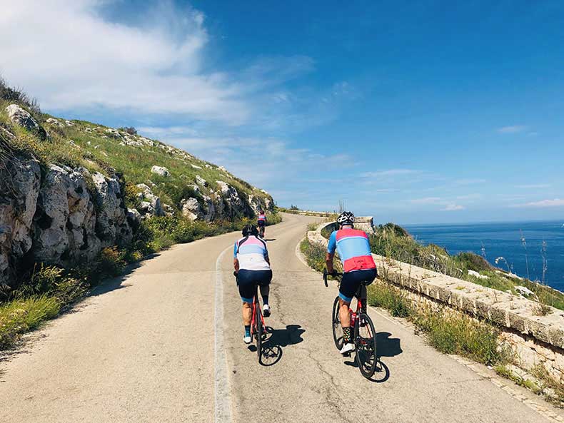 two cyclist riding along the rugged Southern Italian coastline with the Mediterranean at their shoulder