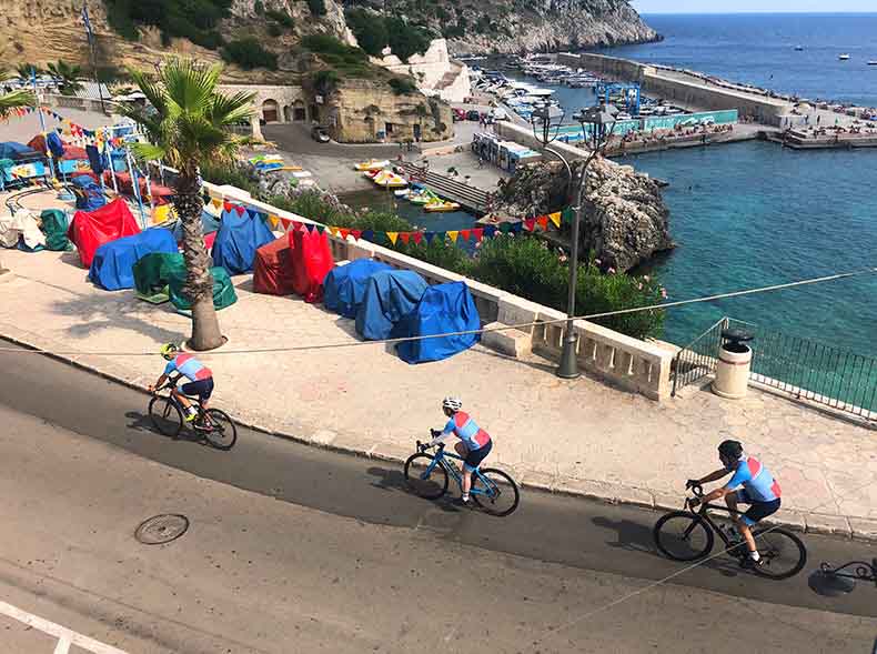 Three riders cycling past in the sea in Puglia