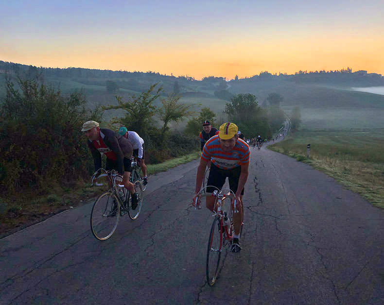 Two riders cycling up a hill at dawn