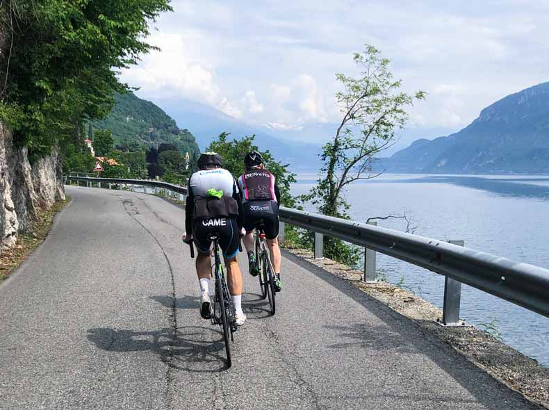 Two cyclists riding along the edge of Lake Como in Italy