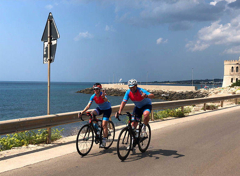 Two riders cycling by the coast in Italy