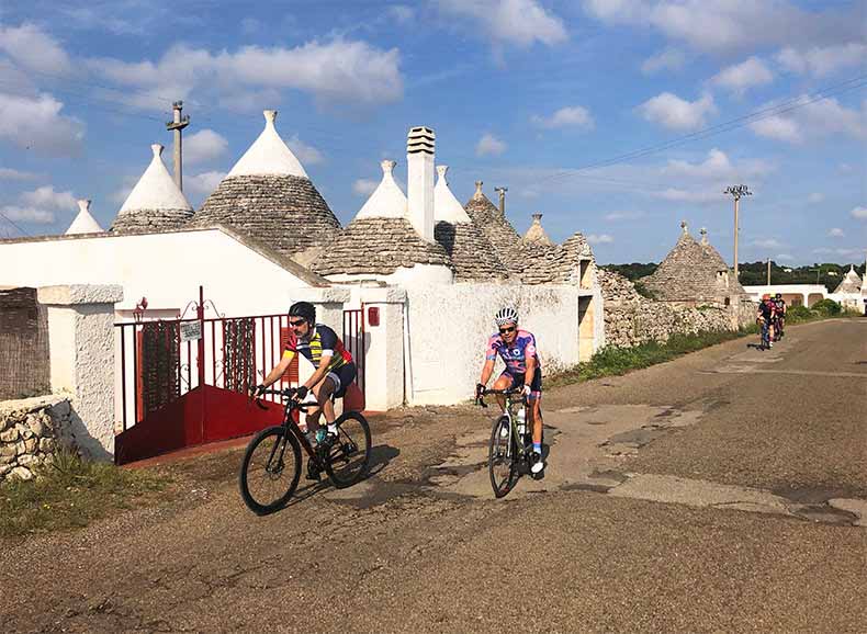 Two riders cycling past trulli in Puglia