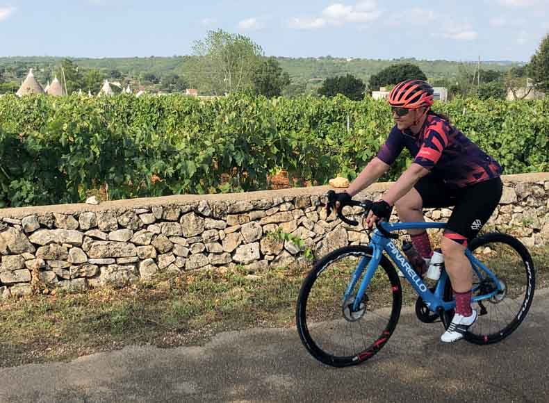 a woman cycling past a rock walled lined vineyard in Puglia