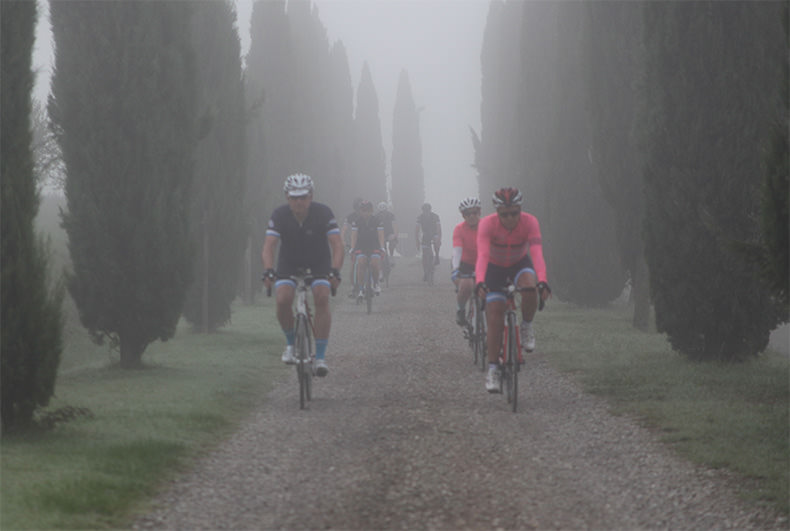 A group of riders cycling on gravel in the fog