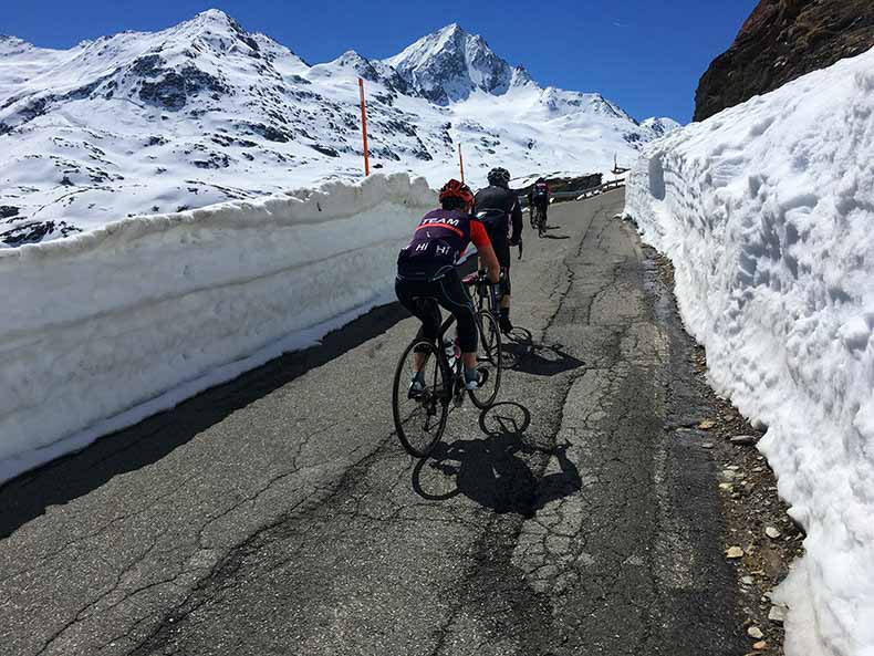 Three riders cycling up Passo Gavia with walls of snow