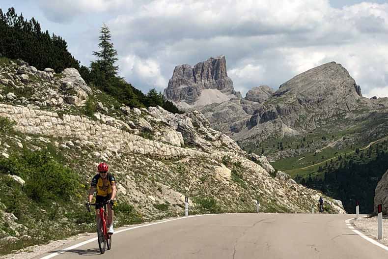 A man cycling to the top of Passo Valporola with the Dolomiti mountains in the background