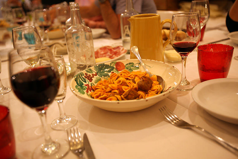 a rustic italian dinner table in Puglia with glasses of wine and pasta and meatballs