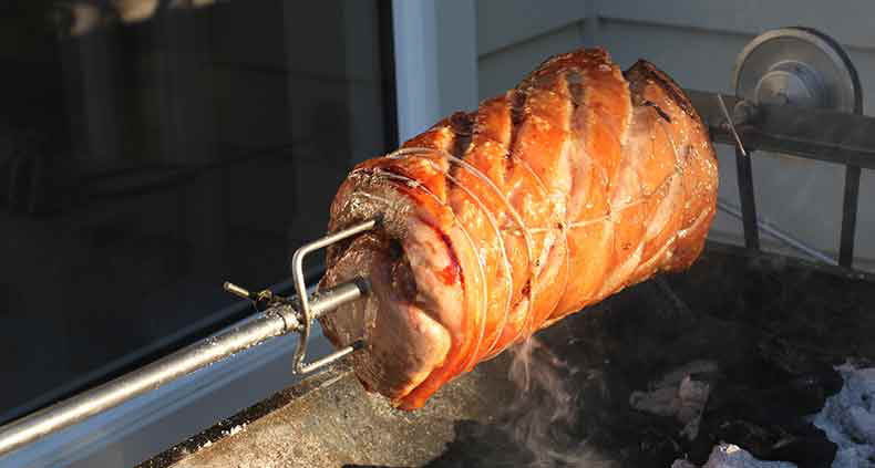 porchetta being slowly cooked on a spit over charcoal