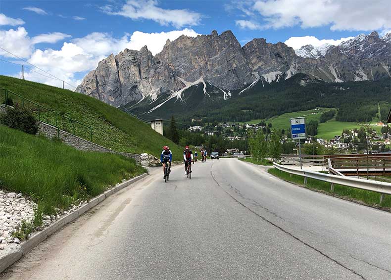 two cyclist riding up a hill with the dolomite mountain in the background