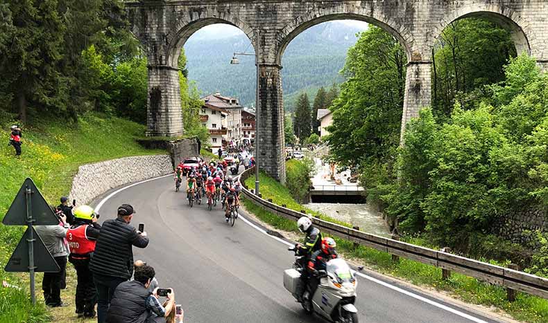 The giro g'Italia race passing underneath a bridge in Cortina d"ampezzo