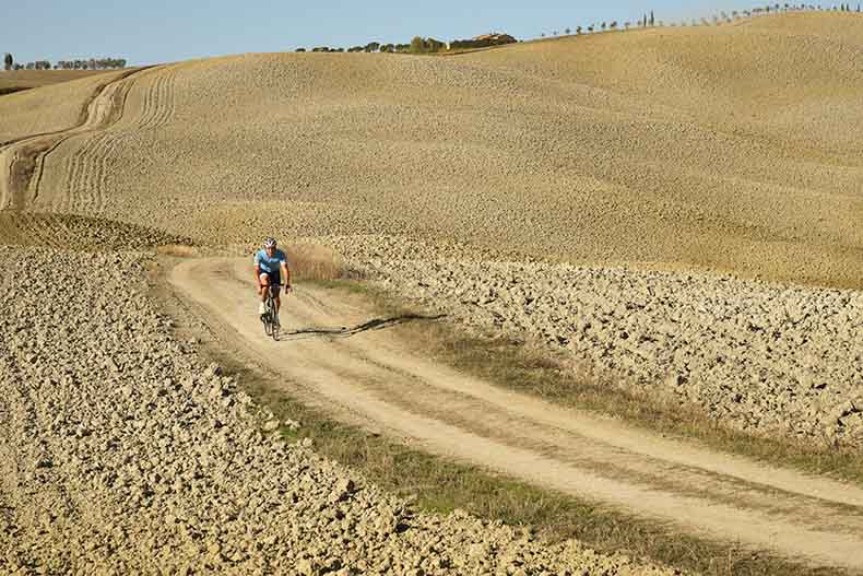 a cycling riding on the barren roads of the Val d Orcia