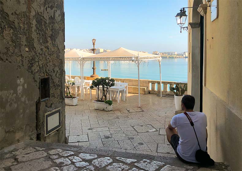 A man sitting on a step looking at the water in Otranto