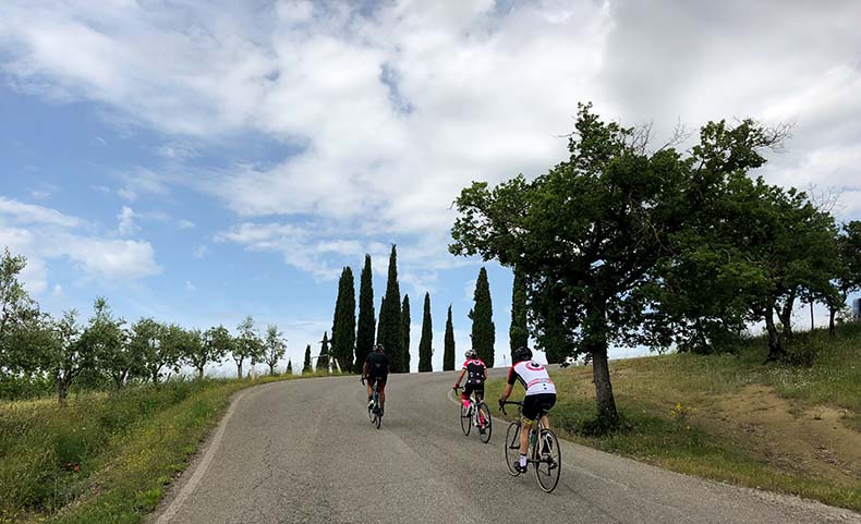 Three riders cycling up a steep hill in Tuscany