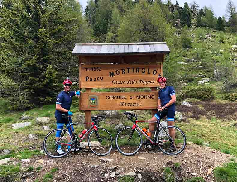 Two cyclists and their bikes beside the Passo Mortirolo sign